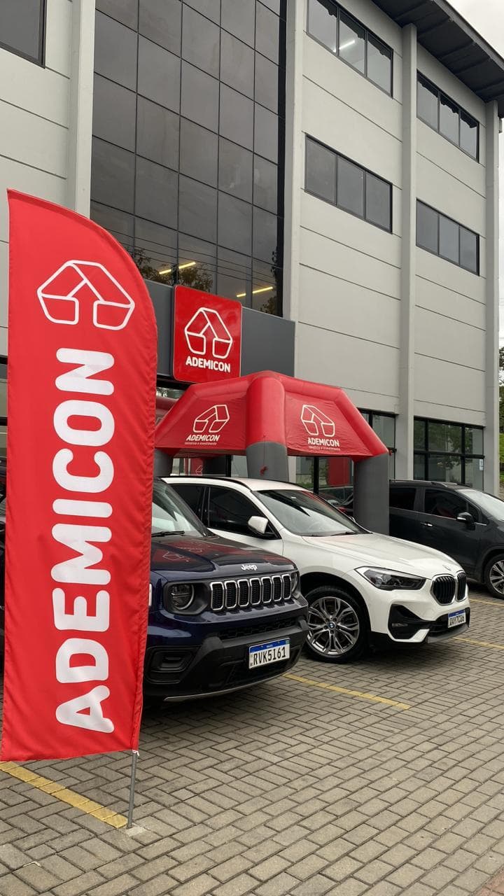 Fachada da unidade Ademicon Joinville no bairro Santo Antônio, com wind banner da marca, tenda inflável e carros no estacionamento